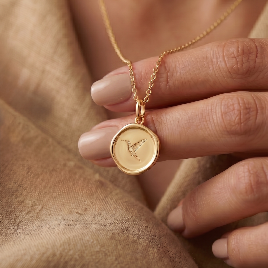 Gold necklace with a pendant held by a hand against a neutral background