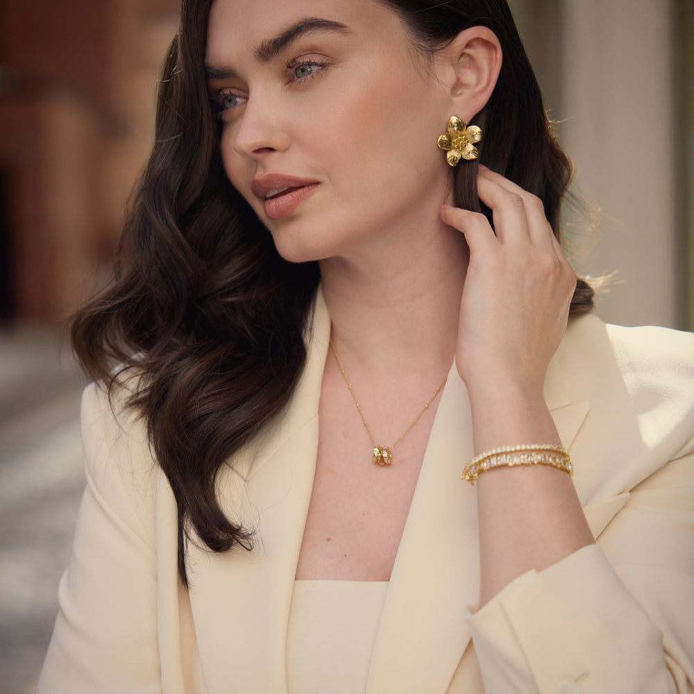 Woman wearing gold jewelry, including earrings and a bracelet, in an outdoor setting.