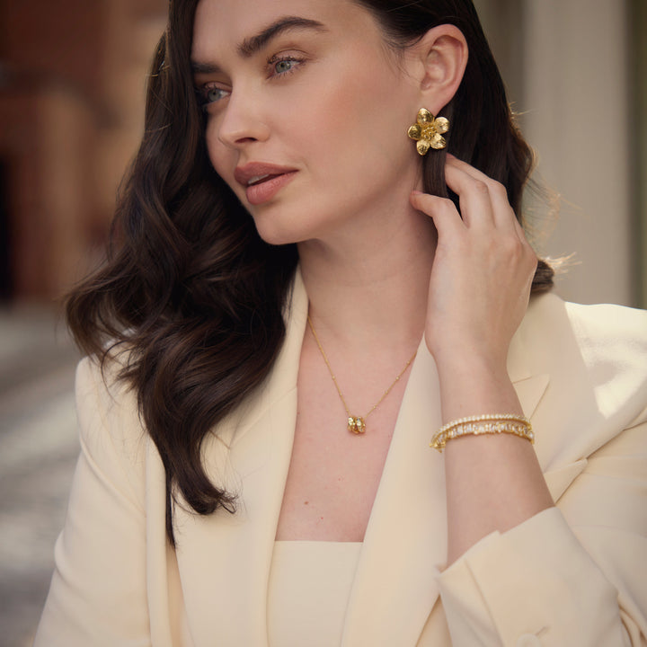 Woman wearing gold jewelry, including earrings and a bracelet, in an outdoor setting.