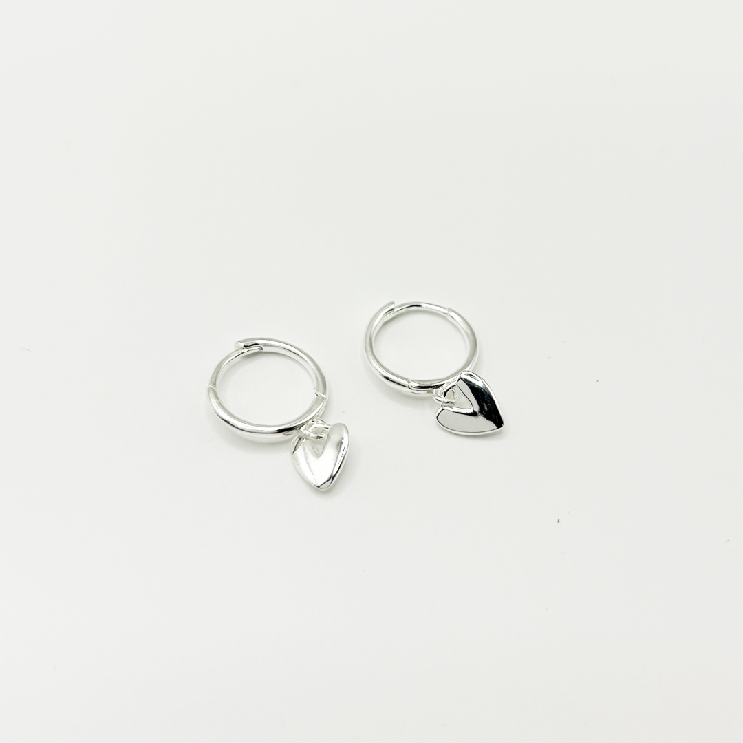 Pair of silver hoop earrings with heart-shaped charms on a light gray background
