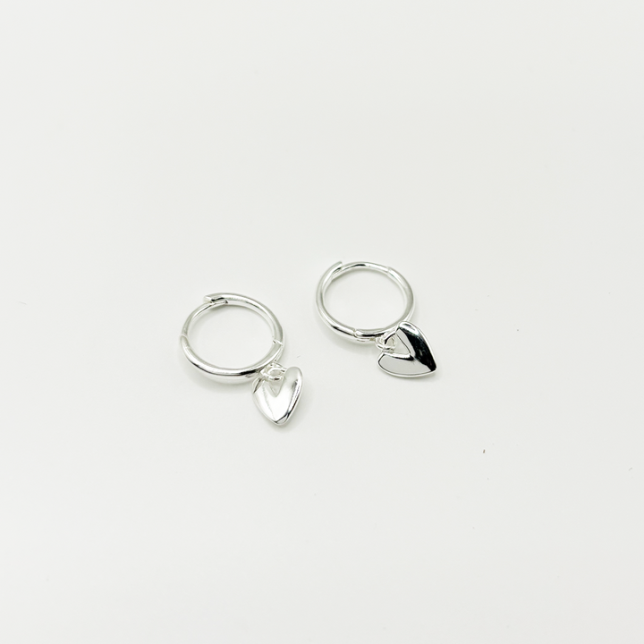 Pair of silver hoop earrings with heart-shaped charms on a light gray background