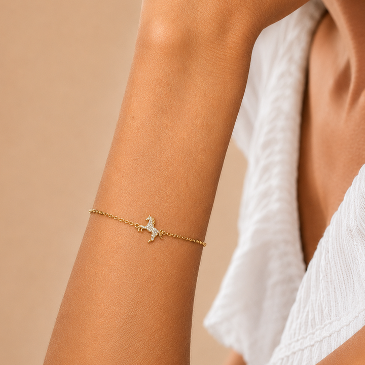 Gold bracelet with a horse charm on a person's wrist against a beige background